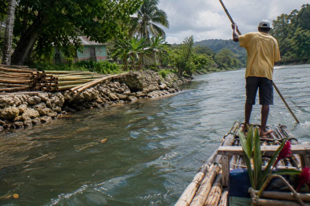 A river captain standing at the rear of a bamboo raft steering with a long pole